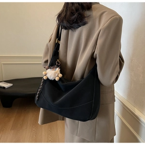 Detail of black half-moon shoulder bag with plush bear charm worn with casual suit