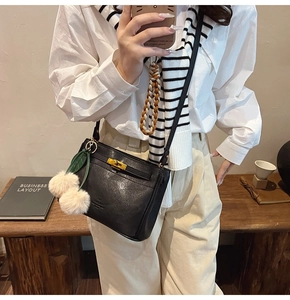 Detail of black leather handbag with gold twist lock and plush pom-pom charms