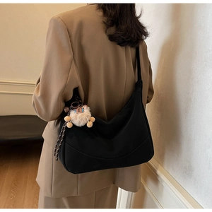 Detail view of black crescent dumpling bag with a cute plush lion charm on model
