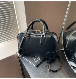 Detail view of black leather Boston bag with gold zippers and adjustable strap