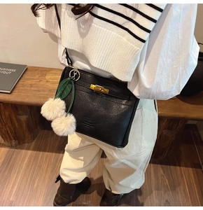 Detail of black leather Kelly style bag with gold hardware and cherry plush charm