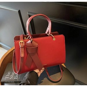 Elegante rote strukturierte Ledertasche mit dekorativer Schleife und goldener Aufschrift