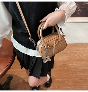 Dettaglio della mini borsa bowling marrone con ciondolo a fiocco e tracolla rimovibile