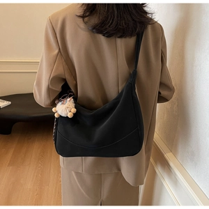 Detail of a black crescent shoulder bag with a cute beige plush bear charm
