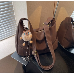 Detailed view of brown crescent shoulder bag with plush charm and golden buckle hardware