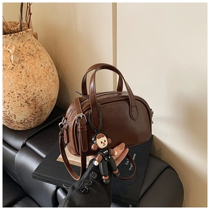 Nahaufnahme der braunen Vintage-Leder-Henkeltasche mit Cartoon-Anhänger auf einer Lederbank