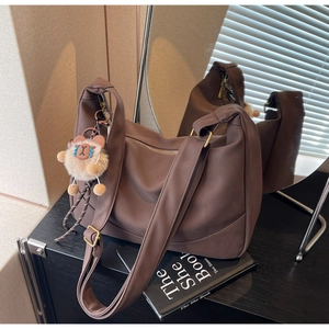 Detail of dark brown dumpling bag with wide shoulder strap and plush bear pendant
