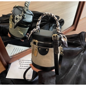 Detailed mirror shot of a two-tone bucket bag with scarf-wrapped handle and gold charms