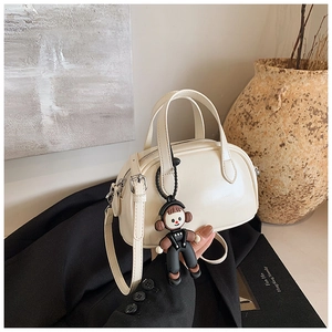 Detail einer cremeweißen Boston Bag mit Cartoon-Anhänger auf einer schwarzen Jacke