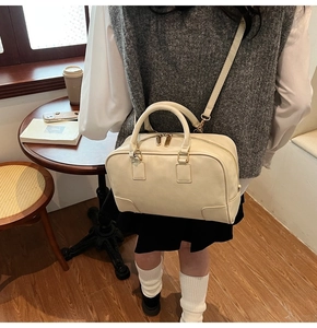 Detail of a creamy white Boston bag with gold hardware shown in a cafe setting
