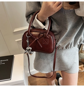 Borsa bowling rosso scuro con grande fiocco e ciondolo a cuore indossata da una modella