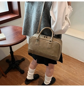 Close-up of khaki Boston bag with top handles and adjustable strap in a cafe setting