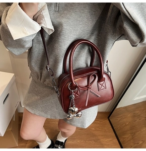Dettaglio borsa bowling rossa vintage con fiocco in pelle e ciondolo a cuore su modella