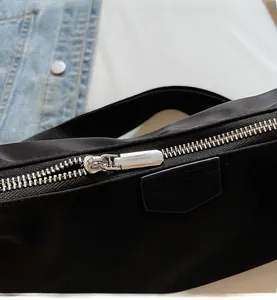 Detail of silver metal zipper and leather logo patch on black nylon shoulder bag