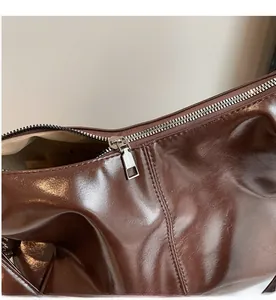 Close-up of a smooth silver zipper and glossy dark brown leather finish on a tote bag