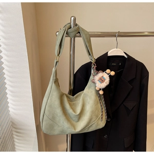 Detail of grey-green suede hobo bag with wide strap and cute plush doll pendant
