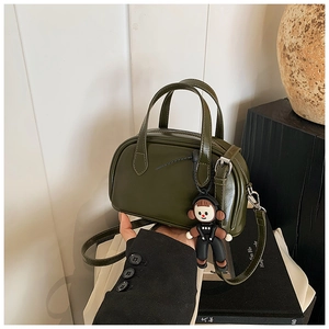 Detailaufnahme der olivgrünen Boston-Tasche aus Leder mit Cartoon-Anhänger und Schultergurt