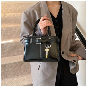 Close-up of black glossy patent leather handbag with gold key charm and buckle detail