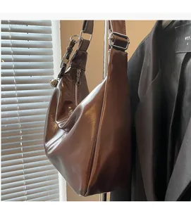 Detail of glossy brown faux leather shoulder bag with wide strap and metallic buckle