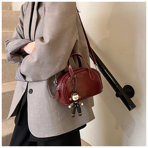 Detailansicht der weinroten Mini-Boston-Tasche mit Lederfinish und süßem Puppenanhänger