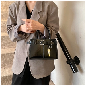 Detail of black glossy handbag featuring gold key pendant and polished patent leather