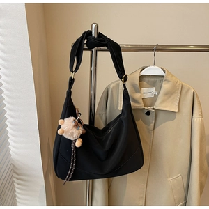 Detail view of black nylon crescent bag with wide strap and plush cat charm on hanger