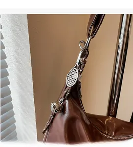 Detail of brown leather tote featuring a tennis racket charm and silver bell accent