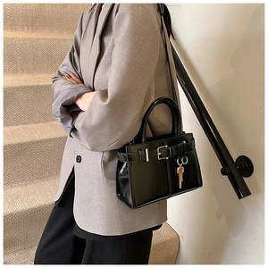 Detail of a black patent leather handbag with gold key pendant and buckle strap decoration
