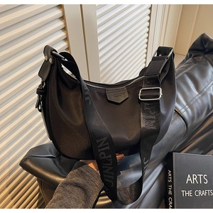 Detail of black nylon crescent shoulder bag with wide adjustable logo strap and leather tag