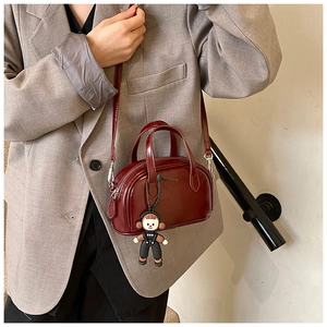 Detail der burgunderroten Lackledertasche mit Trageriemen und niedlichem Puppenanhänger