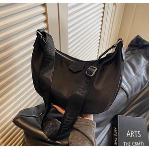 Detail of black crescent moon bag with wide woven strap and logo patch in casual setting