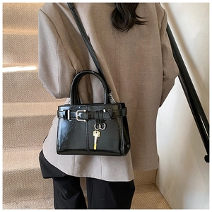 Detail view of black glossy leather handbag with silver buckle and gold key pendant