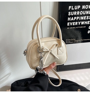 Dettaglio della mini borsa bowling crema con fiocco 3D e ciondolo a cuore in metallo