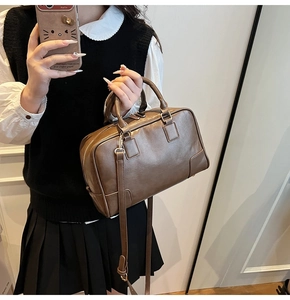 Detail of brown leather Boston bag showing dual top handles and reinforced base patches
