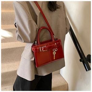 Detail of red patent leather handbag with decorative metal buckle and key charm