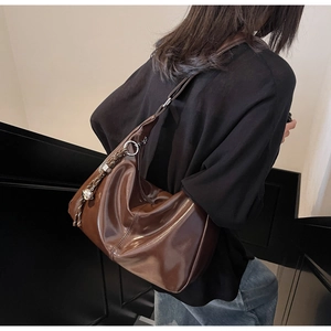 Side view of a dark brown glossy hobo bag with a woven tassel charm on a model