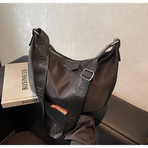 Close-up of black nylon crescent bag featuring wide lettered strap and leather patch