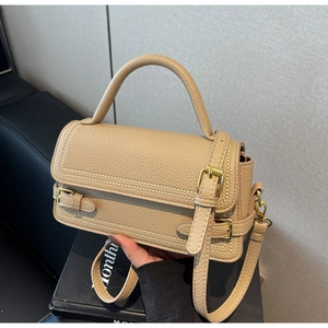 Close-up of beige litchi pattern leather handbag with gold buckle and adjustable strap