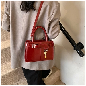 Detail of red glossy patent leather handbag with gold key charm on a beige suit