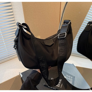 Detail of black nylon dumpling bag featuring wide branded strap and smooth zipper texture