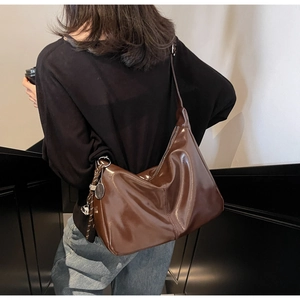 Brown glossy leather crescent bag with silver tennis racket charm worn by a model