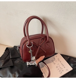 Dettaglio mini borsa bowling bordeaux con fiocco e ciondolo a fiocco in metallo argento