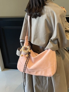 Pink suede-like crescent hobo bag with a cute lion plush pendant on a beige trench coat