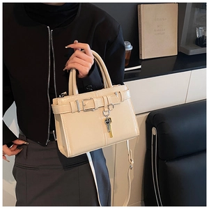 Detail of beige patent leather handbag with metal key charm and structured box design