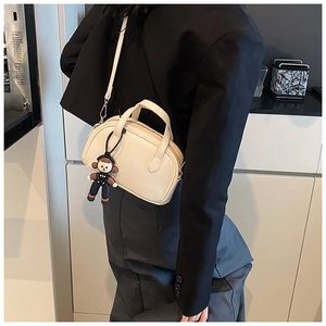 Detail einer cremefarbenen Lederhandtasche mit Griffen und süßem Comic-Anhänger