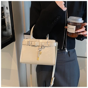 Detail view of cream patent leather handbag featuring gold key charm and crossbody strap