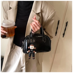 Detail einer mini schwarzen Lacktasche mit einem niedlichen Cartoon-Puppenanhänger für Damen