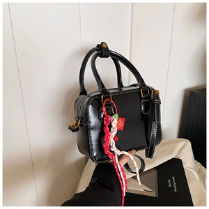 Top-down view of black faux leather Boston bag with colorful lucky charm and gold hardware