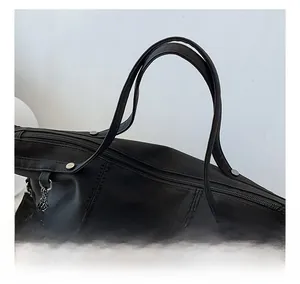Detail of black tote bag featuring metallic rivets, stitched texture and leather tassel