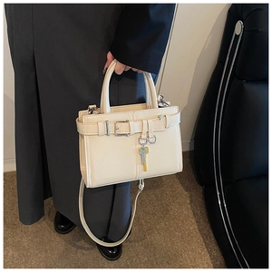 Detailed view of cream leather handbag with gold key charm and stylish belt buckle detail